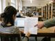 Studentin bespricht am Schreibtisch in der Bibliothek den Entwurf ihrer Bachelorarbeit